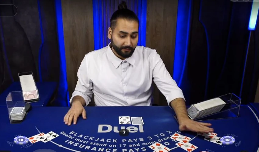 Live-Dealer am blauen Duel-Blackjack-Tisch mit ausgeteilten Karten